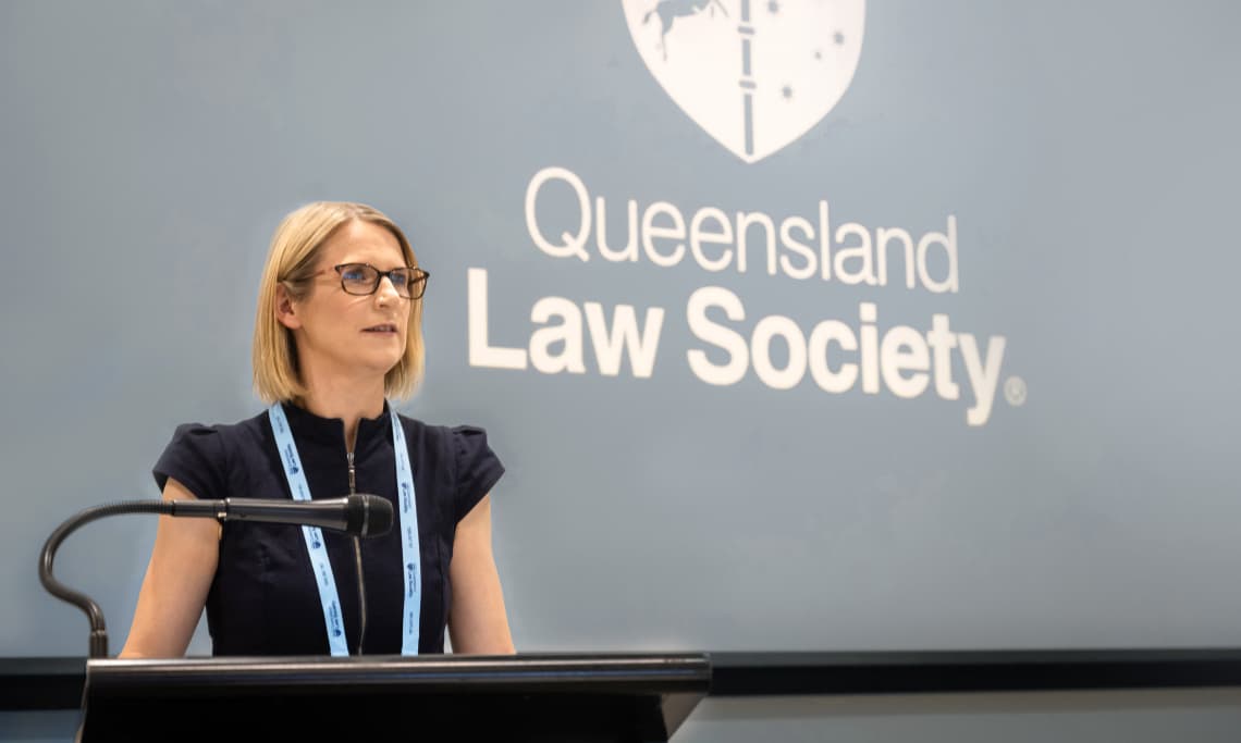 Helen Roebuck presenting at lectern with Queensland Law Society logo on screen